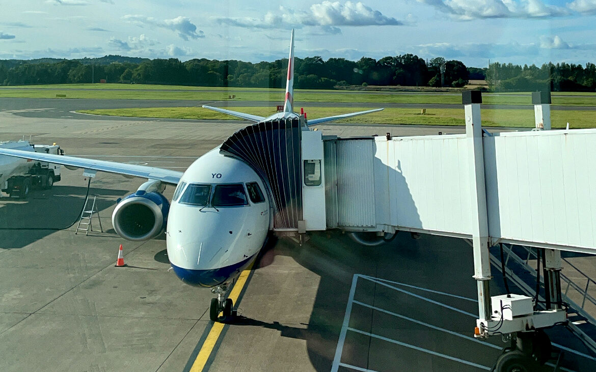 British Airways Plane parked on Airport apron with Jet Bridge attached.
