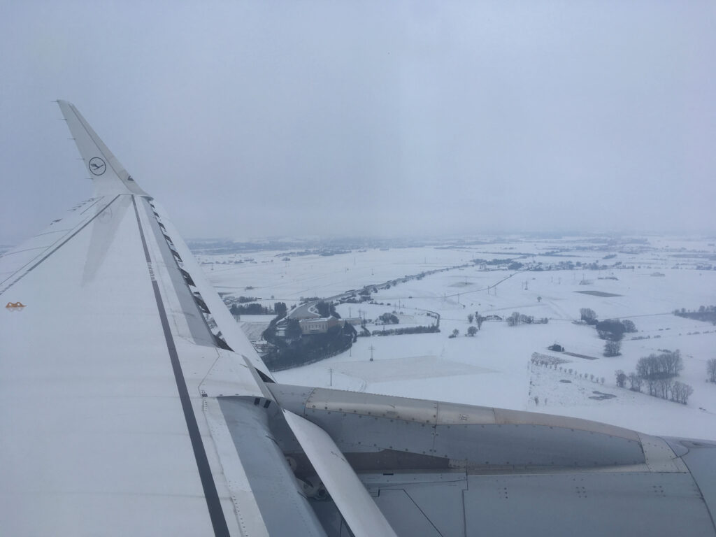 Lufthansa Airplane Wing upon final approach into Munich Airport in Winter. Snow on the ground.