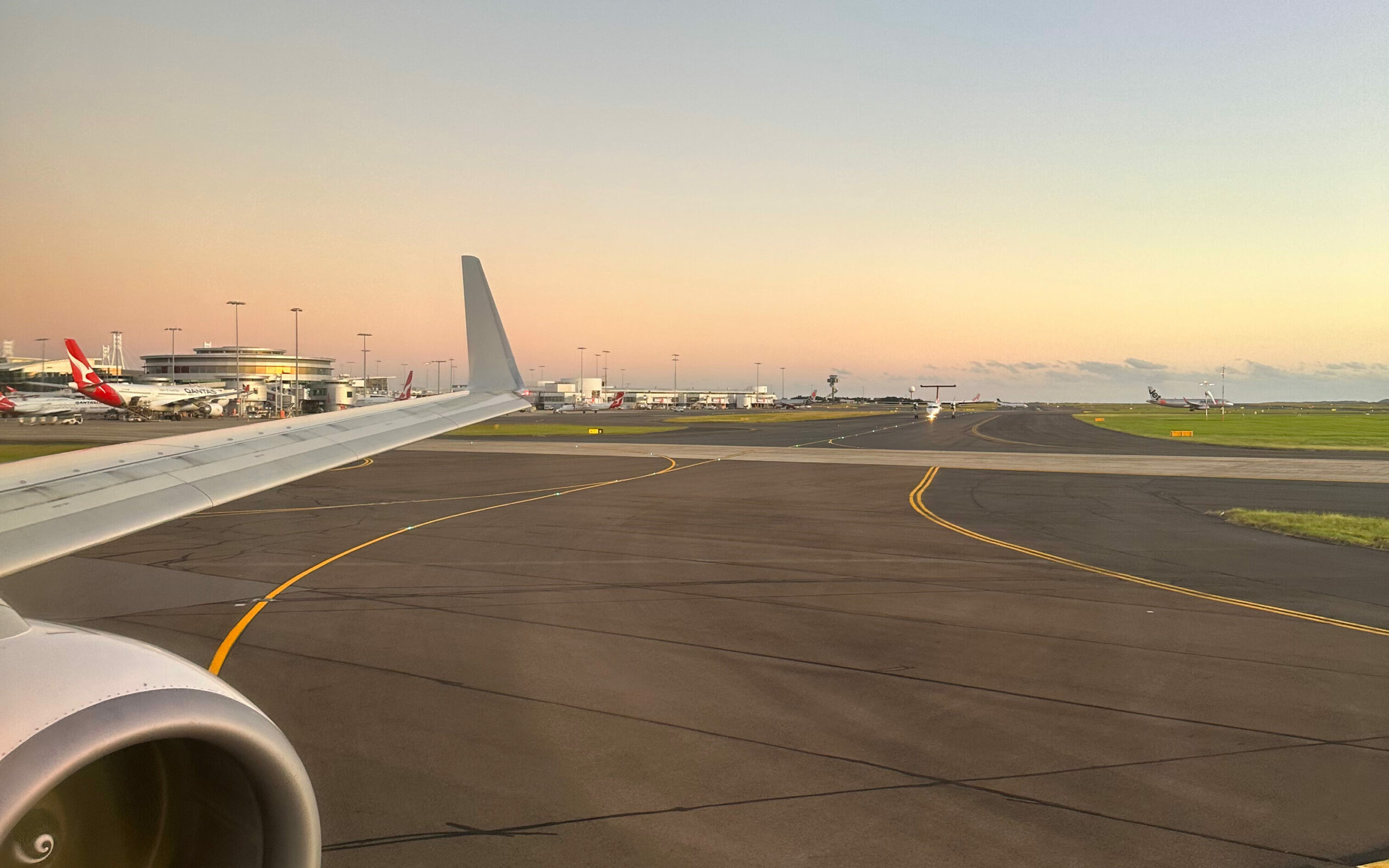 Sunset view from airplane of Sydney International Airport, with Qantas tailfin on a parked aircraft.